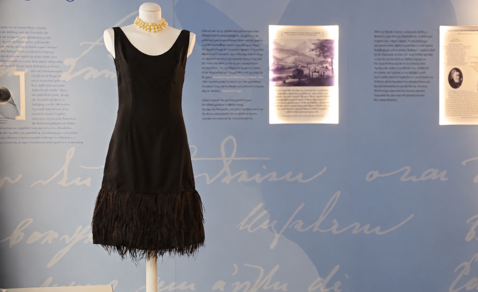 Schwarzes Kleid vor einer Ausstellungswand, digital bearbeitet ohne Personen und Kleiderständer